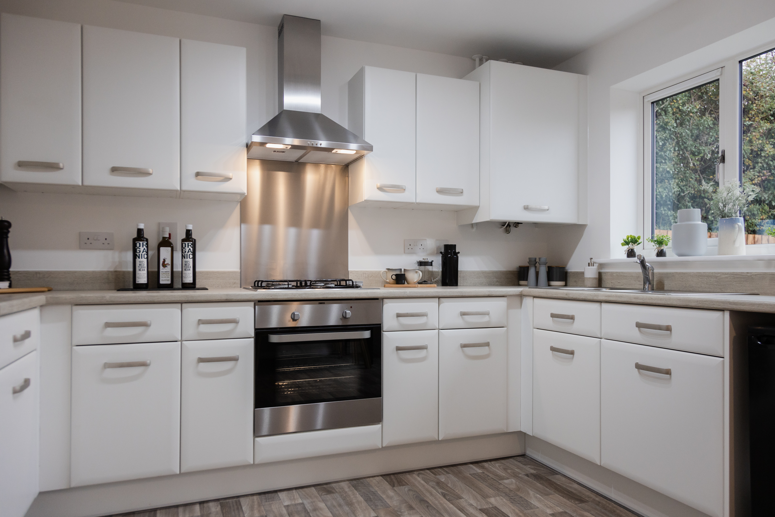 A modern kitchen with white door front, stone colour worktops and stainless steel accessories.